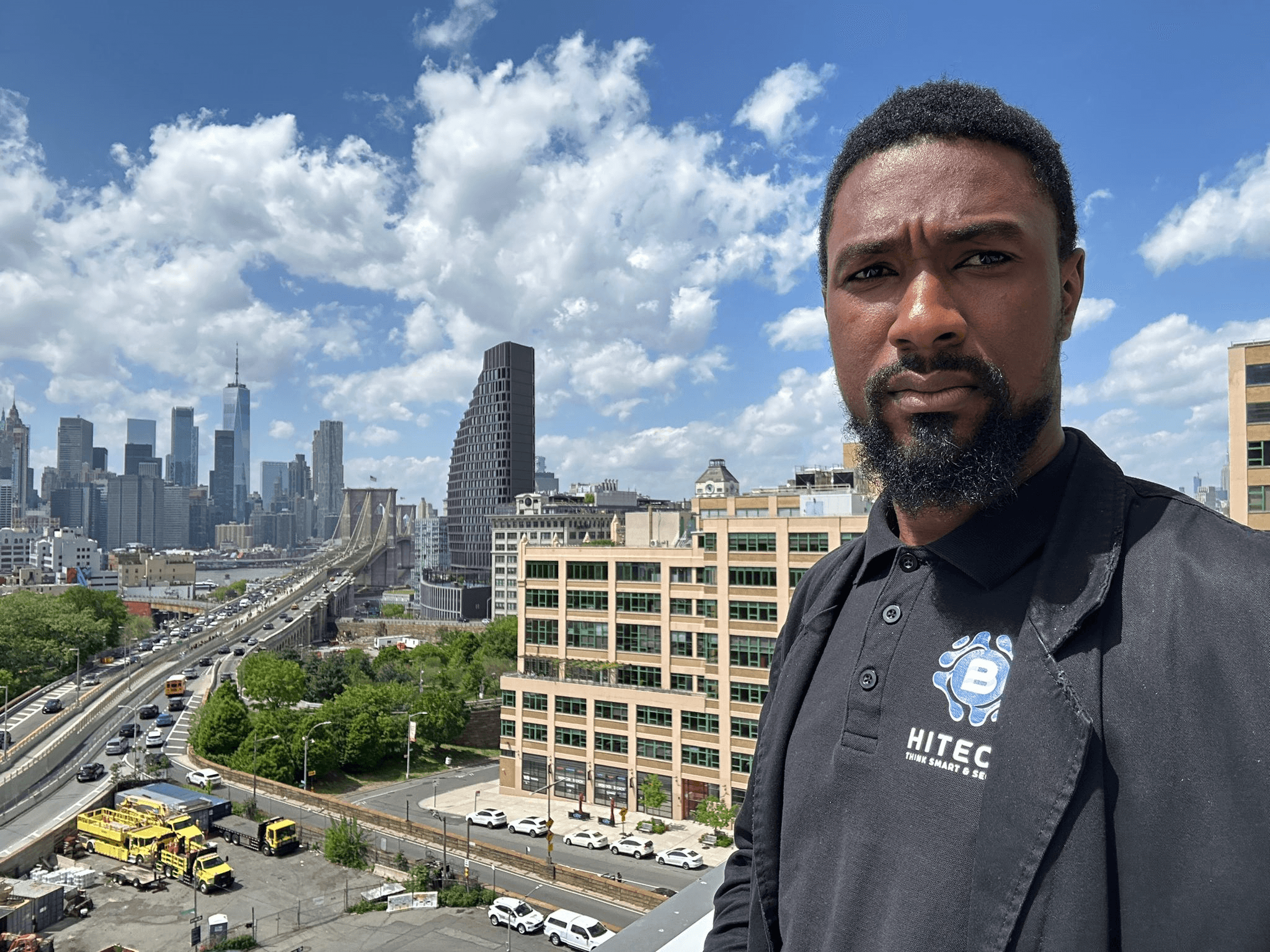 A member of the B-HiTech team in a company shirt, with the New York City skyline behind him