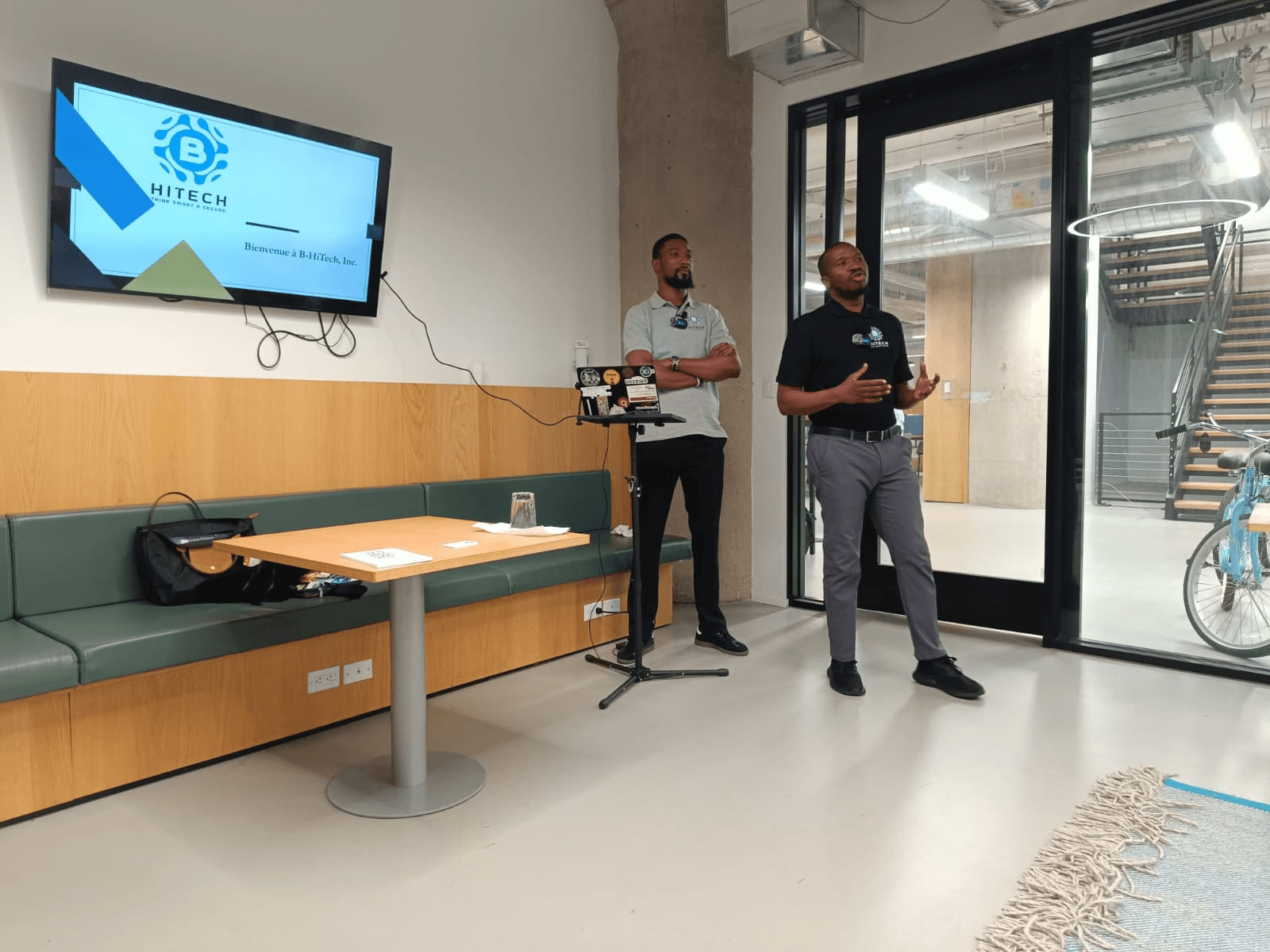 Two members of the B-HiTech team presenting, with the B-HiTech logo on the screen behind them